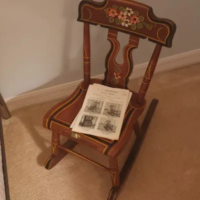 Sale Photo Thumbnail #179: Hand-painted vintage child's wooden rocking chair featuring floral motifs, displayed with a vintage J.A. Ebersol catalog.
