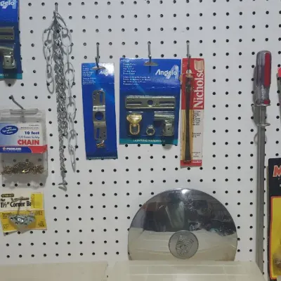 Sale Photo Thumbnail #355: Pegboard selection of various vintage hand tools and hardware, including Angelo lighting hardware packages, a Magna torch, hacksaw blades, chains, and a chrome hubcap.