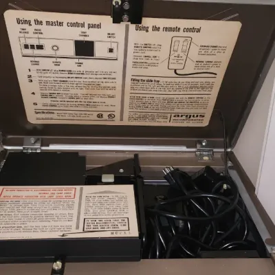Sale Photo Thumbnail #285: Vintage Argus 35mm slide projector in a brown hard-shell case with original operating instructions attached to the inside lid.