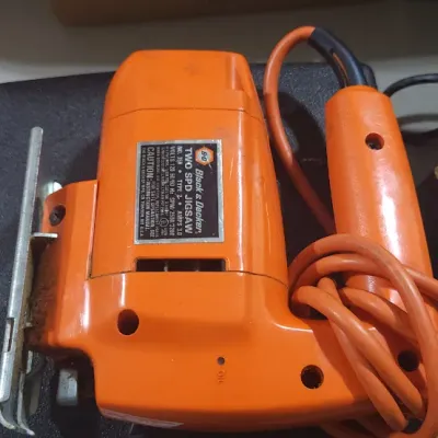 Sale Photo Thumbnail #368: Vintage orange Black & Decker two-speed jigsaw with power cord alongside other hand tools and supplies.