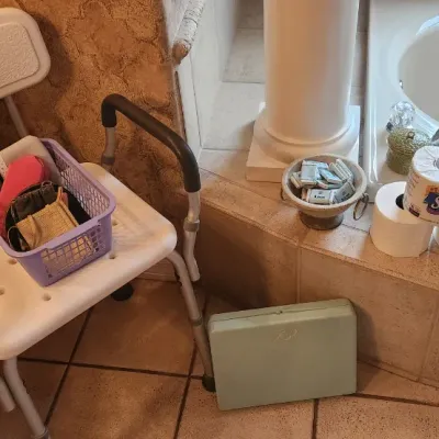 Sale Photo Thumbnail #119: White plastic adjustable shower chair with padded armrests, shown alongside bathroom accessories and a vintage green scale.
