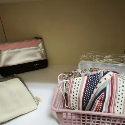 Sale Photo Thumbnail #57: Collection of personal accessories including a silver and pink wristlet pouch, small zippered bags, and a basket filled with patterned cloth face masks.