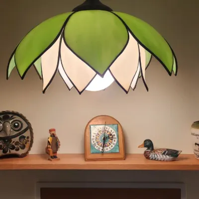 Sale Photo Thumbnail #260: Vintage green and white stained glass lotus-style hanging lamp illuminated above a shelf displaying collectible figurines, a clock, and ceramic jugs.