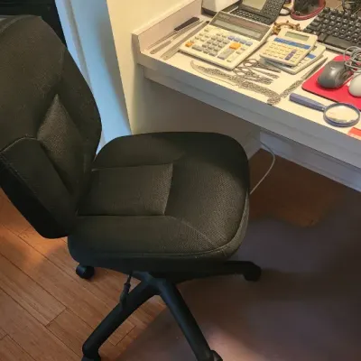 Sale Photo Thumbnail #258: Black fabric armless swivel office chair featuring a five-star caster base alongside a desk filled with office supplies.