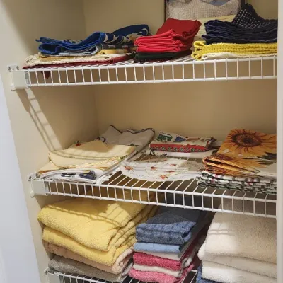 Sale Photo Thumbnail #128: Linen closet filled with organized bath towels, washcloths, placemats, and tablecloths on wire shelving.