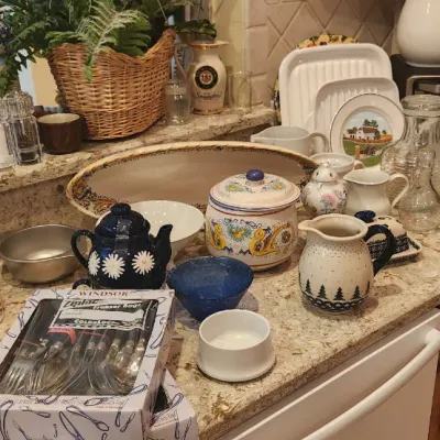 Sale Photo Thumbnail #214: A kitchen counter array of home goods including Italian pottery, teapots, boxed flatware, pitchers, stemware, and small kitchen appliances.