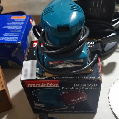 Sale Photo Thumbnail #378: Makita BO4550 corded finishing sander sitting atop its original box, displayed alongside a Craftsman rotary tool and other workshop items.