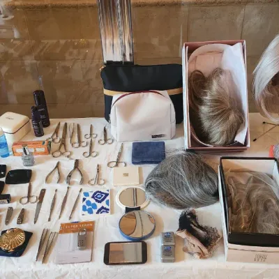 Sale Photo Thumbnail #122: An assortment of personal care and beauty items, including wigs, makeup, grooming tools, mirrors, and cosmetic bags arranged on a table.