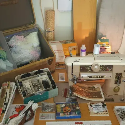 Sale Photo Thumbnail #196: Vintage Singer Slant-O-Matic 401A sewing machine surrounded by assorted crafting supplies, yarn in a vintage suitcase, and notions.