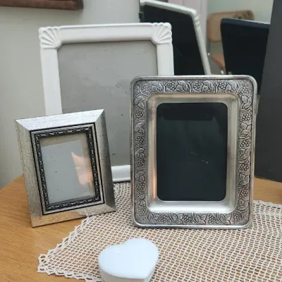 Sale Photo Thumbnail #300: Collection of assorted picture frames, including embossed silver-tone and carved white styles, displayed alongside decorative frosted glass egg ornaments.