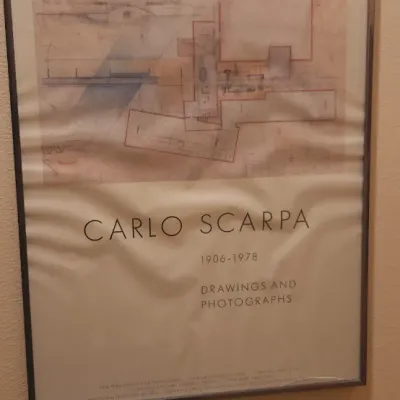 Sale Photo Thumbnail #135: Framed exhibition poster for Carlo Scarpa: Drawings and Photographs, featuring architectural sketches in a thin metal frame with noticeable paper warping.