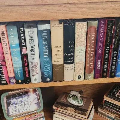Sale Photo Thumbnail #267: Wooden bookshelf filled with various hardback and paperback books, framed photo, and decorative items.
