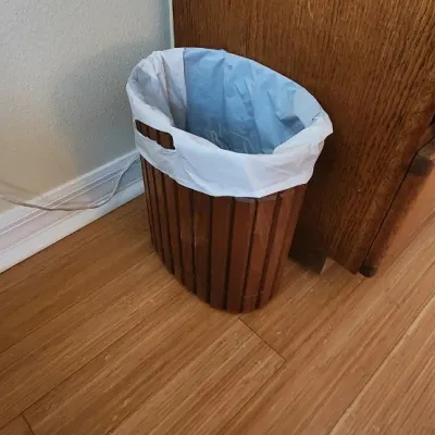 Sale Photo Thumbnail #110: Oval wooden slat trash can with integrated side handles, lined with a plastic bag.