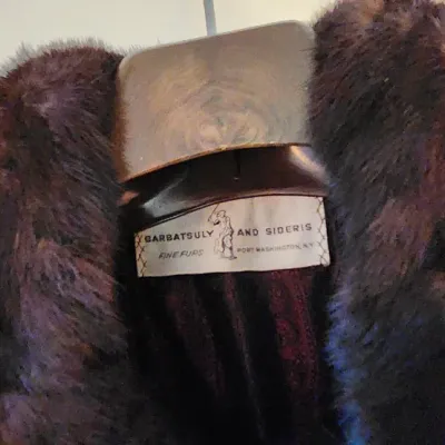 Sale Photo Thumbnail #94: Vintage Barbatsuly and Sideris fur collar coat, hanging on a wooden hanger with a visible maker's tag.
