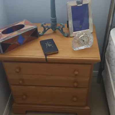 Sale Photo Thumbnail #183: Light oak wooden two-drawer nightstand holding decor items, including a stained glass tissue box cover, small book, picture frame, and table clock.