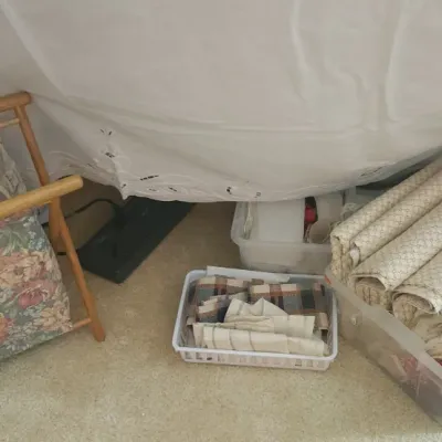 Sale Photo Thumbnail #188: Collection of crafting and sewing supplies, including a floral wooden magazine rack, rolls of fabric, and storage bins under a table cloth.