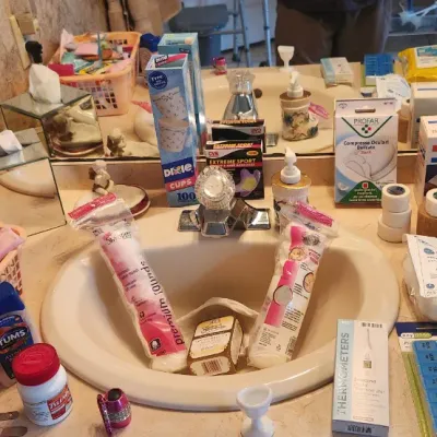 Sale Photo Thumbnail #116: Assortment of bathroom, health, and personal care items including medical supplies, toiletries, and hair styling tools displayed on a vanity counter.