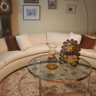 Sale Photo Thumbnail #27: Large cream-colored curved sectional sofa with throw pillows surrounding a circular glass-top coffee table in a living room setup.