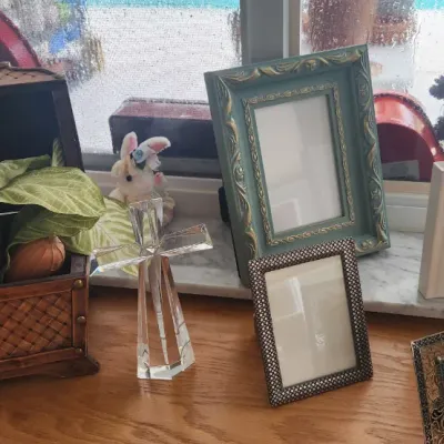 Sale Photo Thumbnail #273: Collection of home decor items including decorative picture frames, a crystal standing cross, an Anne Geddes book, and a small woven trunk with faux foliage.