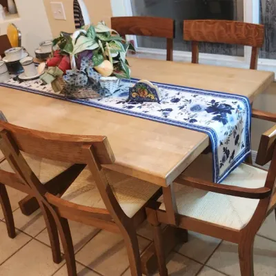 Sale Photo Thumbnail #242: Light wood dining table set with six matching wooden chairs featuring rush-style woven seats, styled with a blue and white patterned runner.