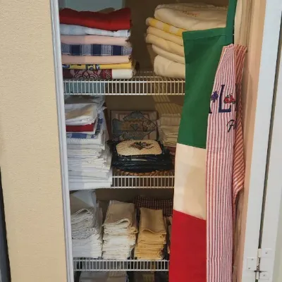Sale Photo Thumbnail #231: Linen closet filled with organized household textiles, including folded tablecloths, towels, blankets, and hanging aprons.