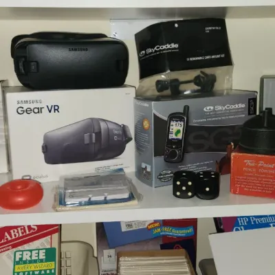 Sale Photo Thumbnail #281: Collection of small electronics and tech accessories including a Samsung Gear VR headset, Roku Premiere+, SkyCaddie GPS, TomTom GPS, and a Verbatim external CD/DVD writer.