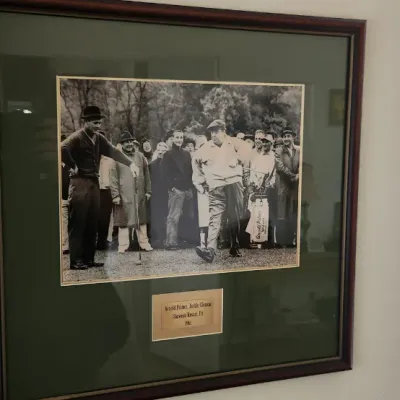 Sale Photo Thumbnail #276: Framed black-and-white photograph depicting Arnold Palmer and Jackie Gleason on a golf course, mounted with a green mat in a dark wood frame.
