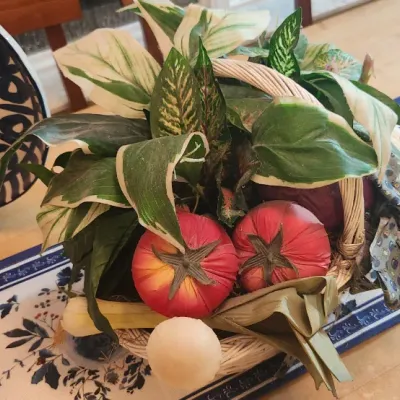 Sale Photo Thumbnail #241: Decorative table centerpieces, including artificial foliage and faux vegetables arranged in a woven basket, alongside a black and white patterned ceramic platter.