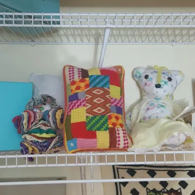 Sale Photo Thumbnail #191: Wire closet shelf holding a Tiffany & Co. box, handcrafted fabric dolls, a patchwork needlepoint pillow, and crafting supplies including yarn.
