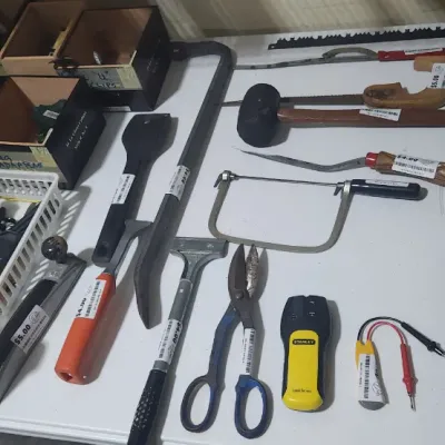 Sale Photo Thumbnail #351: Assortment of hand tools laid out on a white folding table, including a coping saw, pry bar, rubber mallet, tin snips, and a Stanley stud finder.