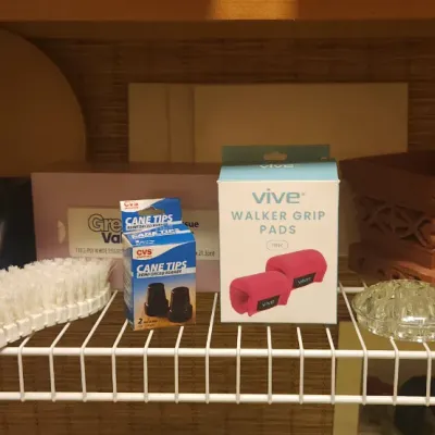 Sale Photo Thumbnail #249: Assorted household goods, mobility aids, and decor including Vive walker grip pads, CVS cane tips, a flashlight, scrub brush, and glass dish arranged on a wire shelf.