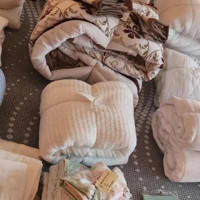 Sale Photo Thumbnail #106: Collection of assorted bedding linens, including embroidered comforters, tied blanket bundles, bed pillows, and packaged vinyl pillow protectors.