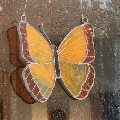 Sale Photo Thumbnail #244: Yellow and brown leaded stained glass butterfly suncatcher hanging in a window.