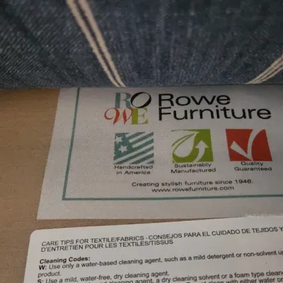 Sale Photo Thumbnail #169: Manufacturer's tag and fabric care label for Rowe Furniture, positioned under a blue striped upholstery cushion.