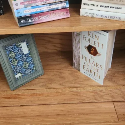 Sale Photo Thumbnail #269: Wooden bookcase filled with various paperback and hardcover books, alongside two decorative picture frames.