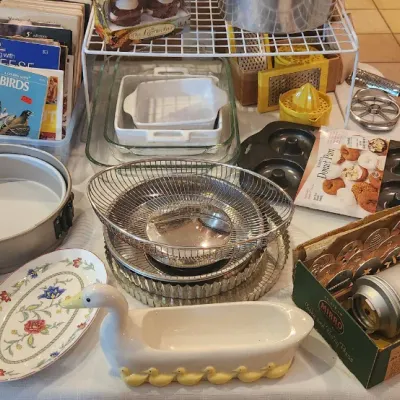 Sale Photo Thumbnail #232: Collection of vintage kitchenware and baking supplies, including a Mirro cookie press in its original box, a duck-shaped planar vessel, cake pans, and various cookbooks.