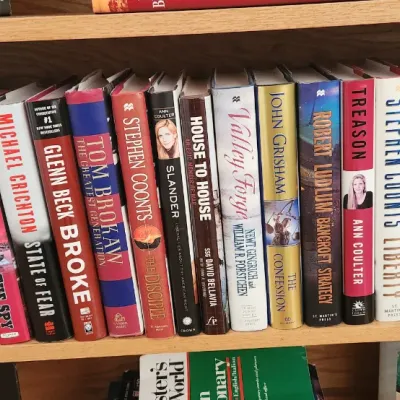 Sale Photo Thumbnail #271: Collection of modern hardcover books on a wooden shelf, including titles by Clive Cussler, Dan Brown, and Stephen Coonts.
