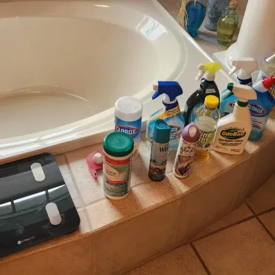 Sale Photo Thumbnail #120: Collection of household cleaning supplies, air fresheners, and bathroom accessories arranged around a large garden bathtub alongside a digital glass scale.