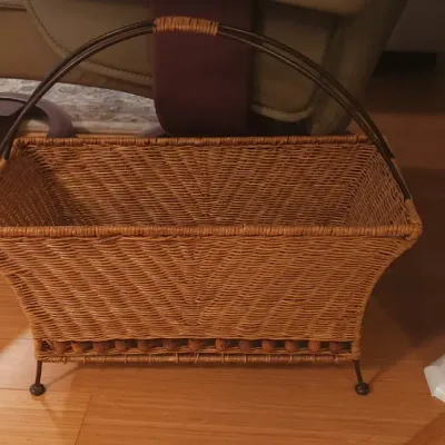 Sale Photo Thumbnail #18: Woven wicker magazine rack with a dark metal arch handle, beaded lower trim, and metal legs.