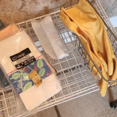 Sale Photo Thumbnail #114: Assortment of household linens and cleaning supplies, including paper guest towels in original packaging and yellow rubber cleaning gloves on a wire organizer.