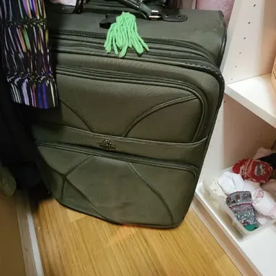 Sale Photo Thumbnail #52: Large dark green softside upright luggage bag with a green yarn tassel tied to the top zipper.