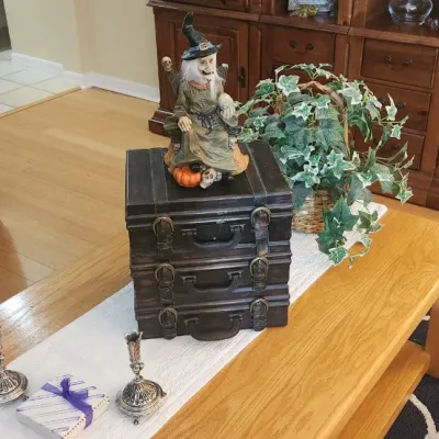 Sale Photo Thumbnail #166: Living room setup featuring an oak coffee table adorned with silver candlesticks, a stacked-trunk decorative box, and a Halloween witch figurine, alongside a blue striped armchair with Cabbage Patch Kids dolls.