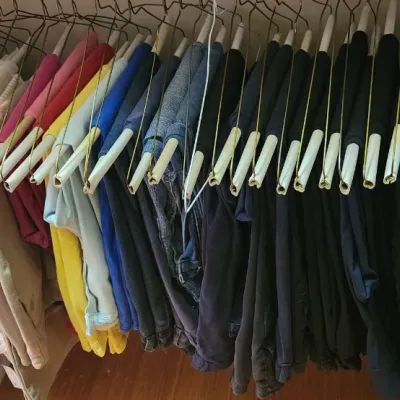 Sale Photo Thumbnail #75: A closet rack full of various colorful and neutral folded pants, including jeans and slacks hanging on wire coat hangers with cardboard tubes.