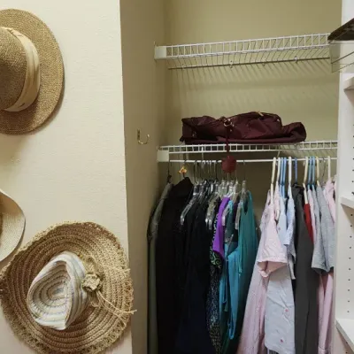 Sale Photo Thumbnail #50: A walk-in closet arrangement featuring woven straw sun hats mounted on the wall alongside hanging women's clothing and open white shelving.