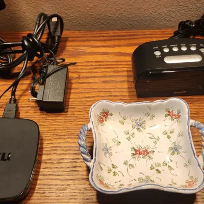 Sale Photo Thumbnail #99: Collection of small electronics and home items including a Roku streaming box, a Sharp alarm clock, a VTech cordless phone handset, and a ceramic floral catchall dish.