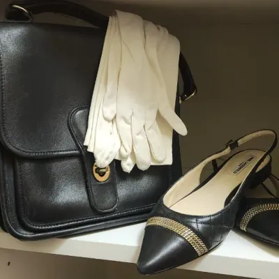 Sale Photo Thumbnail #65: Black leather Coach crossbody bag displayed with a pair of white dress gloves and Karl Lagerfeld chain-detailed slingback flats on a closet shelf.