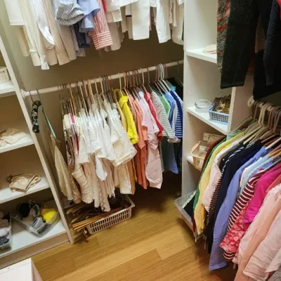 Sale Photo Thumbnail #47: Walk-in closet filled with assorted women's clothing, including shirts, sweaters, and accessories organized on hangers and shelving units.