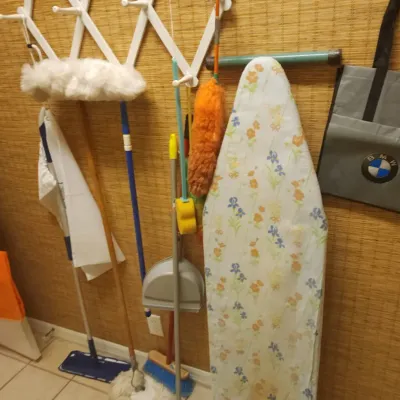 Sale Photo Thumbnail #253: Assorted household cleaning supplies including mops, brooms, a dustpan, an ironing board with a floral cover, and a BMW-branded tote bag.