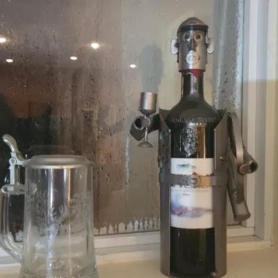 Sale Photo Thumbnail #159: A novelty metal waiter wine bottle holder alongside an etched glass beer stein with a metal lid sitting on a windowsill.