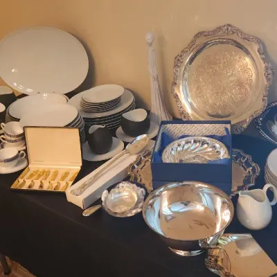 Sale Photo Thumbnail #11: Tabletop display featuring fine china dishware, silver-plated serving trays and bowls, boxed cutlery, and ceramic teacups.